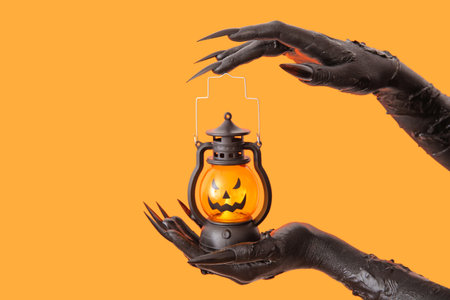Black hands of witch with lantern on orange background. halloween celebration