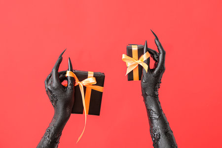 Black hands of witch with gift boxes on red background. halloween celebrationの写真素材