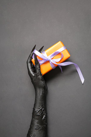 Black hand of witch with gift box on gray background. halloween celebrationの写真素材