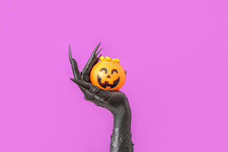 Black hand of witch with cauldron and tasty candy corns on purple background. halloween celebrationの写真素材