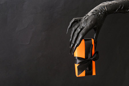 Black hand of witch with gift box on dark background. halloween celebrationの写真素材