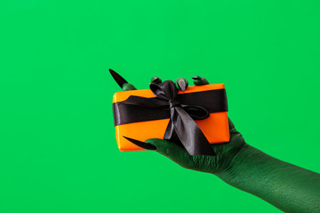 Hand of witch with gift box on green background, closeup. halloween celebrationの写真素材
