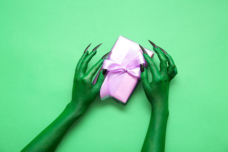 Hands of witch with gift box on green background. halloween celebrationの写真素材