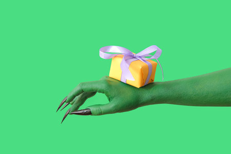 Hand of witch with gift box on green background. halloween celebrationの写真素材