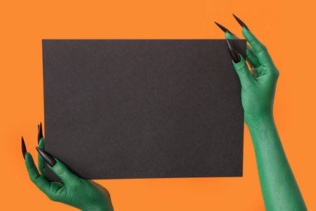 Hands of witch with blank black paper sheet on orange background. halloween celebrationの写真素材