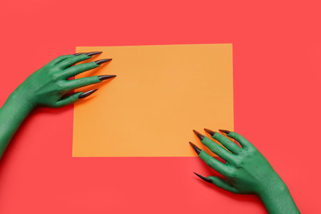 Hands of witch with blank orange paper sheet on red background. halloween celebrationの写真素材