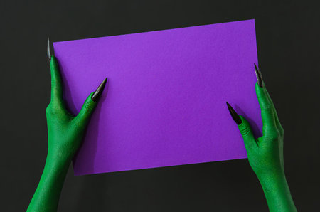 Hands of witch with blank purple paper sheet on dark background. halloween celebrationの写真素材