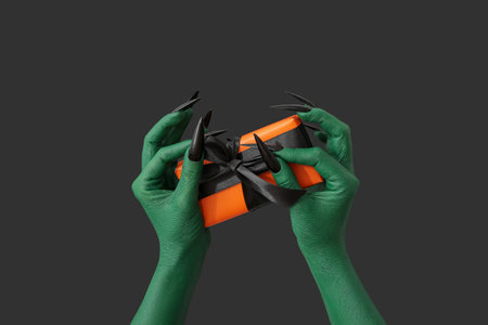 Green hands of witch with gift box on dark background. halloween celebrationの写真素材