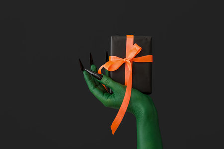 Green hand of witch with gift box on dark background. halloween celebrationの写真素材