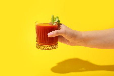 Woman holding glass of tasty tomato juice on yellow backgroundの写真素材