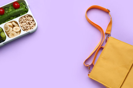 Bag and lunchbox with tasty food on lilac backgroundの写真素材