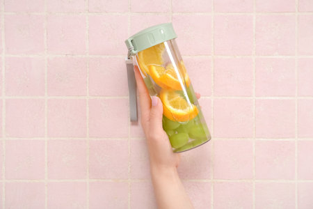 Woman holding bottle of infused water with orange and grapes on pink tile backgroundの写真素材