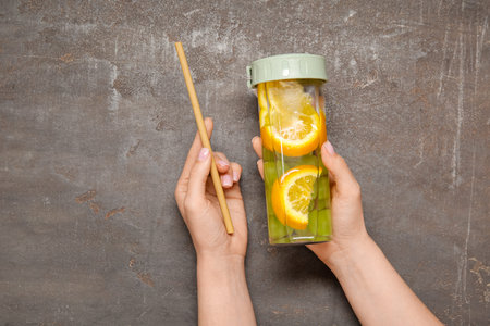 Woman holding bottle of infused water with orange and grapes on dark background