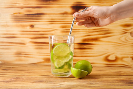 Woman putting straw into glass of infused water with lime on wooden backgroundの写真素材
