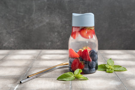 Sports bottle of infused water with blueberries, strawberries and mint on gray tile tableの写真素材