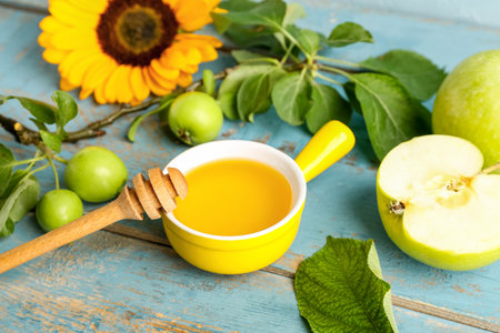 Bowl of honey with apples and sunflower for Rosh Hashanah celebration (Jewish New Year) on blue wooden tableの写真素材
