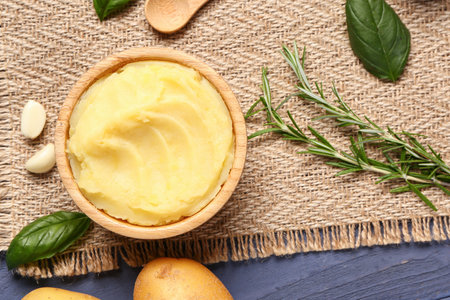 Bowl of tasty mashed potatoes with rosemary and basil on blue wooden backgroundの写真素材