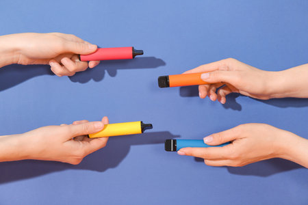 Women holding electronic cigarettes on blue background