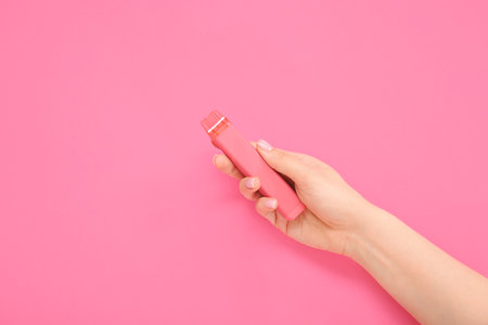 Woman holding electronic cigarette on pink backgroundの写真素材