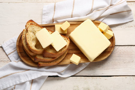 Board with fresh butter and bread on white wooden background