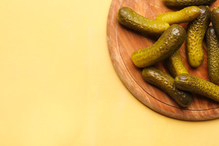 Wooden board with pickled cucumbers on yellow backgroundの写真素材