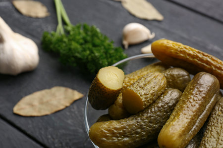 Glass bowl with pickled cucumbers and different spices on black wooden backgroundの写真素材
