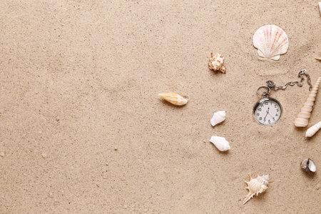 Pocket watch and seashells on sand background
