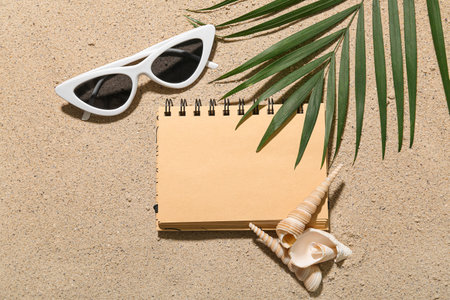 Composition with notebook, sunglasses, seashells and palm leaf on sand backgroundの写真素材