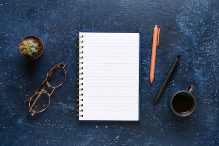 Notebook with eyeglasses and cup of tasty coffee on blue backgroundの写真素材