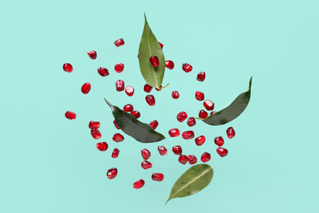 Flying fresh pomegranate seeds and leaves on turquoise backgroundの写真素材