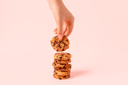 Woman taking tasty cookie with chocolate chips on pink backgroundの写真素材