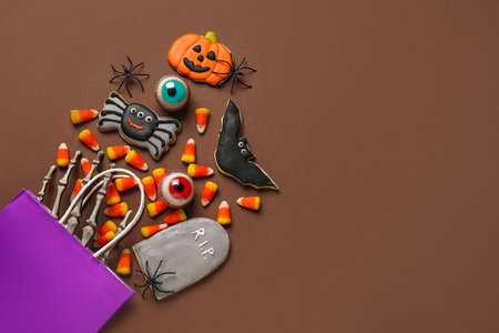 Shopping bag with tasty candy corns, cookies for Halloween and skeleton hand on brown backgroundの写真素材