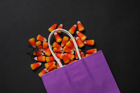 Shopping bag with tasty candy corns and Halloween decor on black backgroundの写真素材