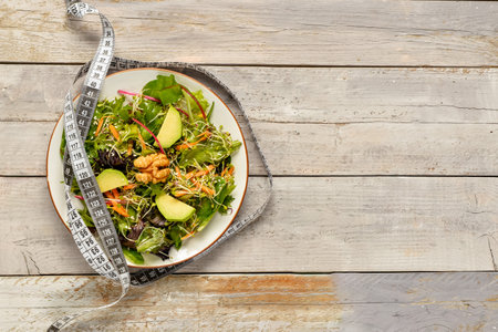 Plate with fresh salad and measure tape on gray wooden background. Diet conceptの写真素材