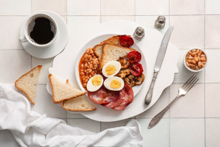 Plate with tasty English breakfast and cup of coffee on white tile backgroundの写真素材