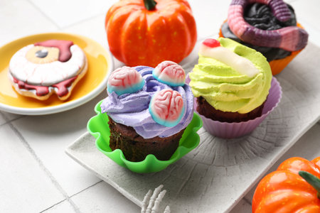 Plate with delicious Halloween cupcakes and candies on light tile background, closeupの写真素材