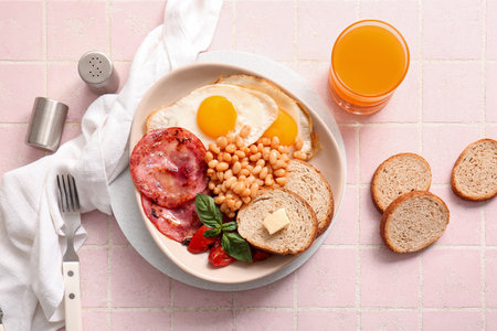 Plate with tasty English breakfast and glass of juice on pink tile backgroundの写真素材
