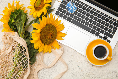 Eco bag with beautiful sunflowers, cup of coffee and modern laptop on light backgroundの写真素材