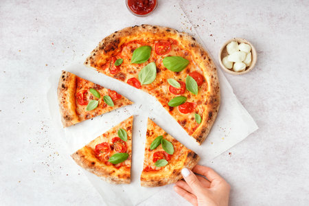 Woman taking piece of tasty pizza Margarita with tomatoes and basil on white tableの写真素材