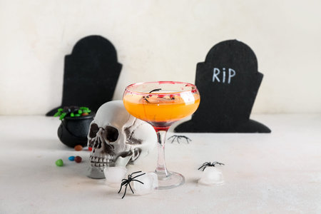 Glass of tasty Margarita cocktail, skull, ice cubes and decorations for Halloween on light backgroundの写真素材