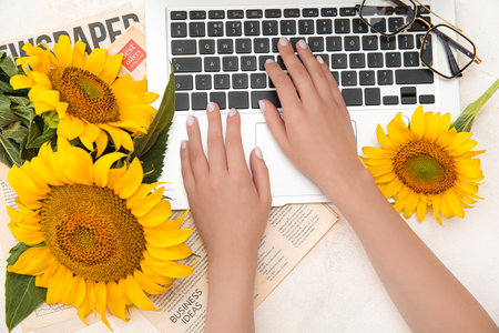 Woman with modern laptop, beautiful sunflowers eyeglasses on light backgroundの写真素材