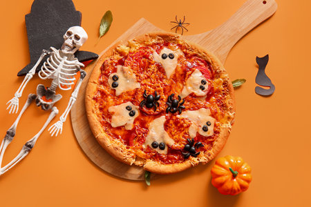 Wooden board with tasty pizza for Halloween celebration on orange backgroundの写真素材