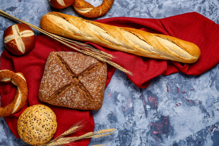 Different types of bread and wheat ears on gray table