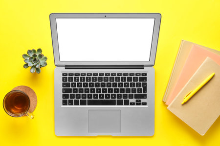 Modern laptop, stationery and cup of tea on yellow background