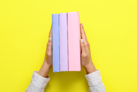 Female hands holding books on yellow backgroundの写真素材