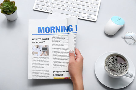 Woman reading newspaper at workplace with cup of coffee on gray backgroundの写真素材