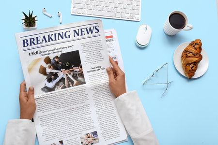 Woman reading newspaper at workplace with coffee and croissant on blue backgroundの写真素材