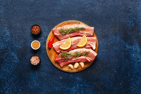 Wooden board with raw pork ribs, rosemary and spices on dark color backgroundの写真素材