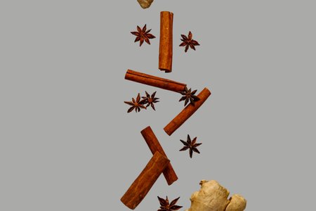 Flying cinnamon sticks, anise stars and ginger root on gray backgroundの写真素材