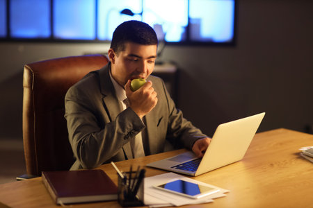 Young businessman eating apple in office at nightの写真素材